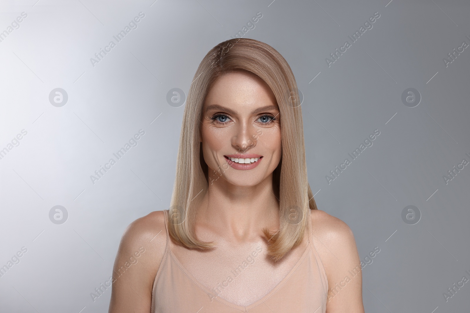 Image of Portrait of attractive woman with blonde hair smiling on grey background