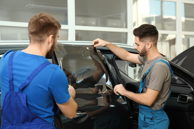 Workers tinting car window with foil in workshop