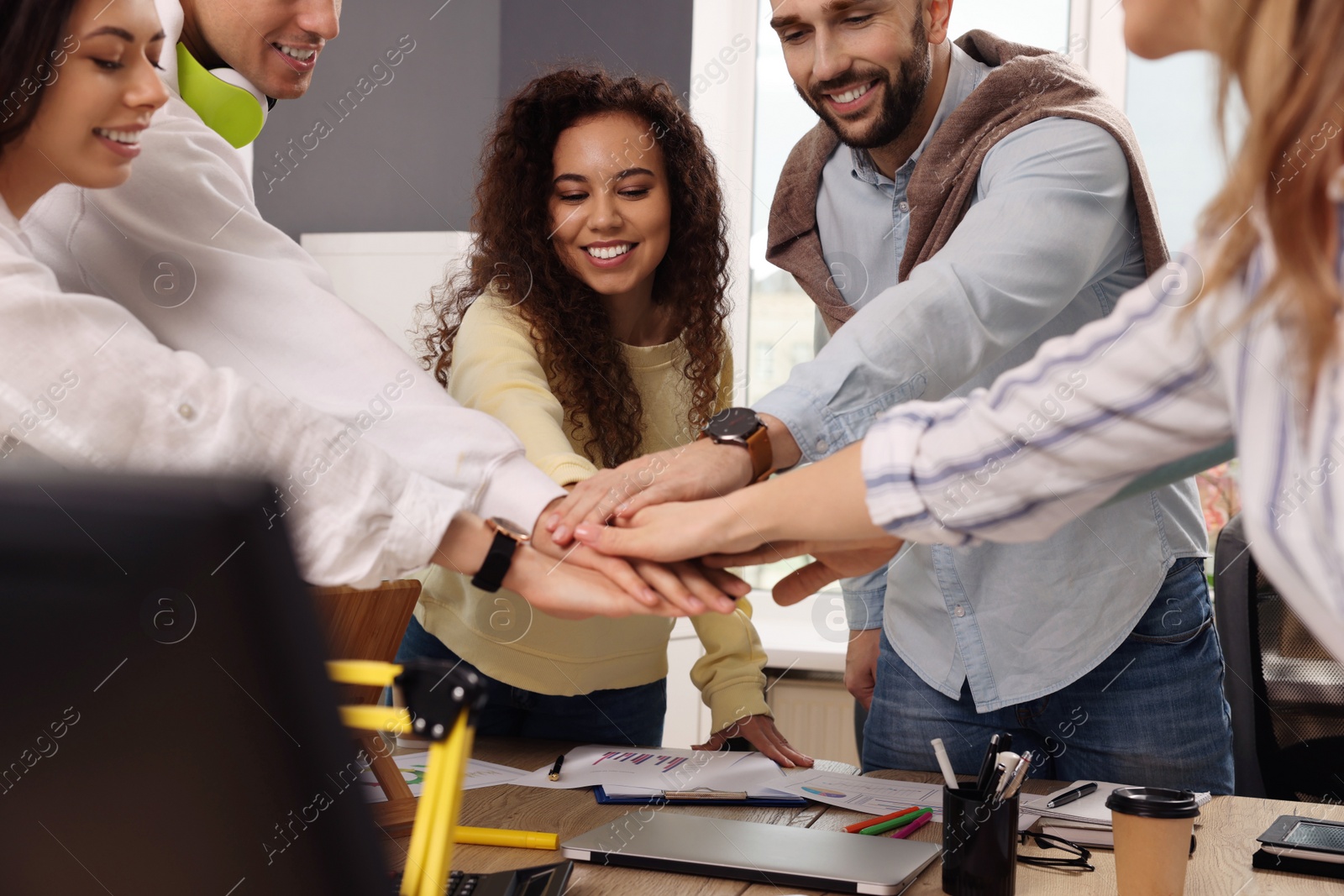 Photo of Team of employees putting hands together in office. Startup project