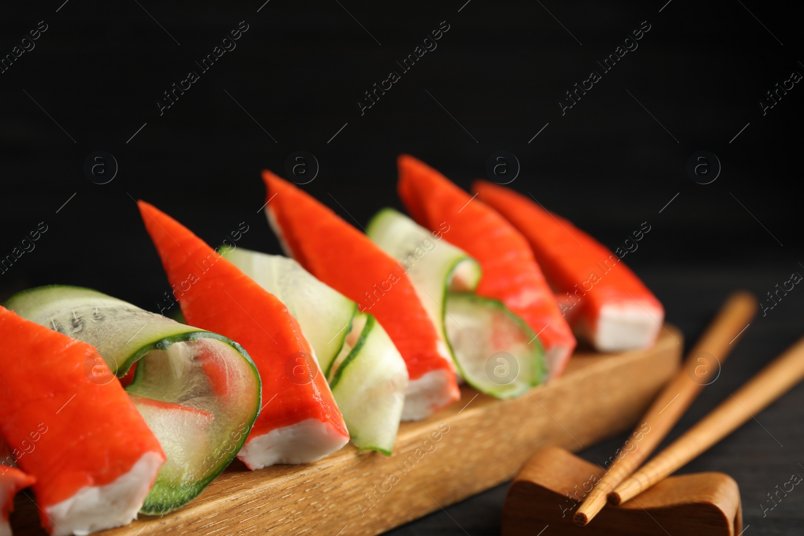 Photo of Cut crab sticks with cucumber on wooden board, closeup