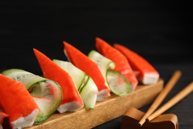 Photo of Cut crab sticks with cucumber on wooden board, closeup