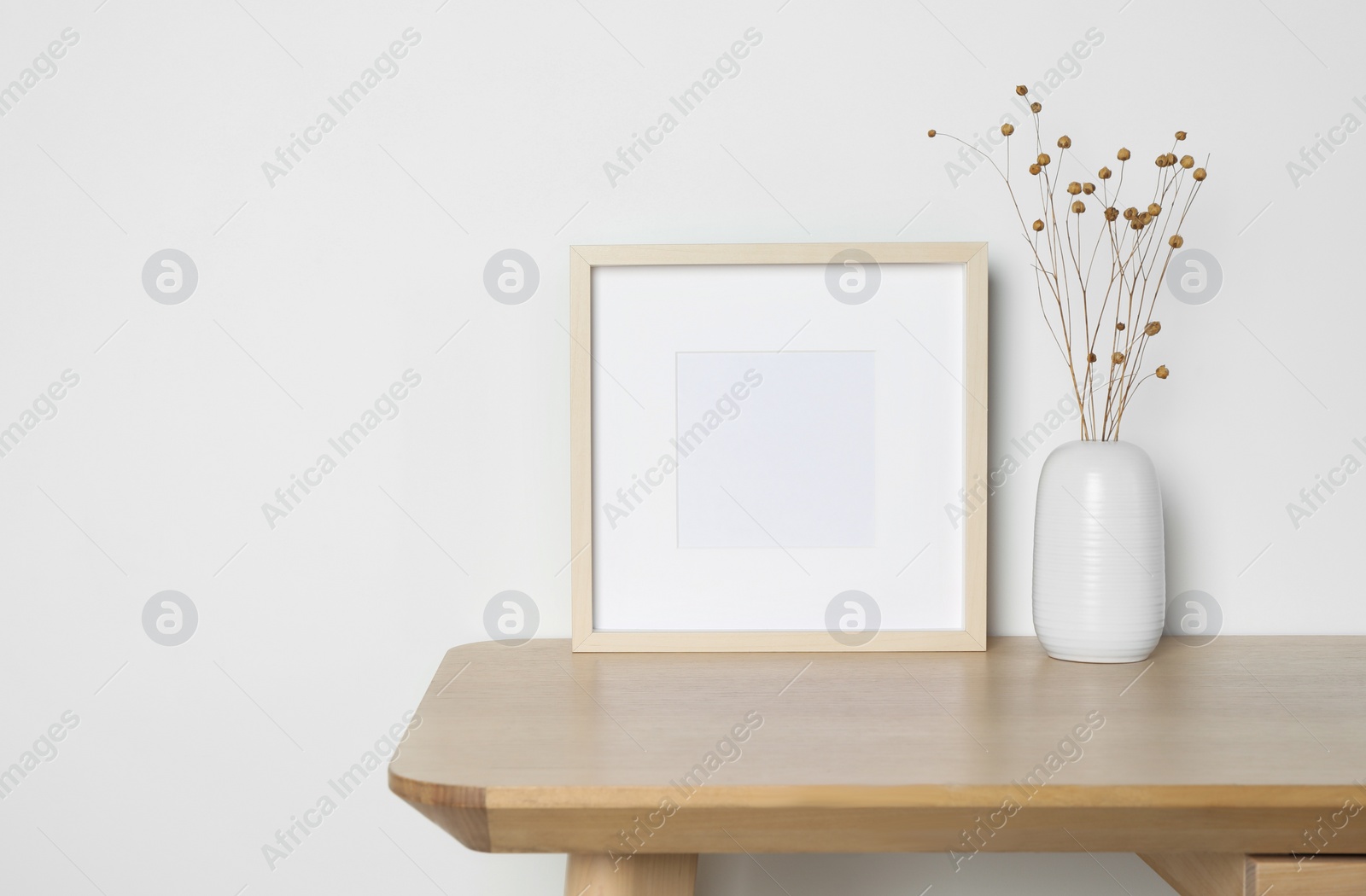 Photo of Empty photo frame and vase with dry decorative flowers on wooden table. Mockup for design