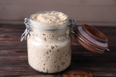 Photo of Sourdough starter in glass jar on wooden table, closeup