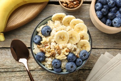 Tasty oatmeal with banana, blueberries and walnuts served in bowl on wooden table, flat lay