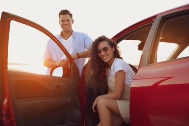 Photo of Happy couple near car outdoors at sunset. Summer trip