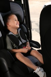 Photo of Little boy fastened with car safety belt in child seat