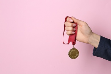 Photo of Woman holding golden medal on color background, closeup. Space for text