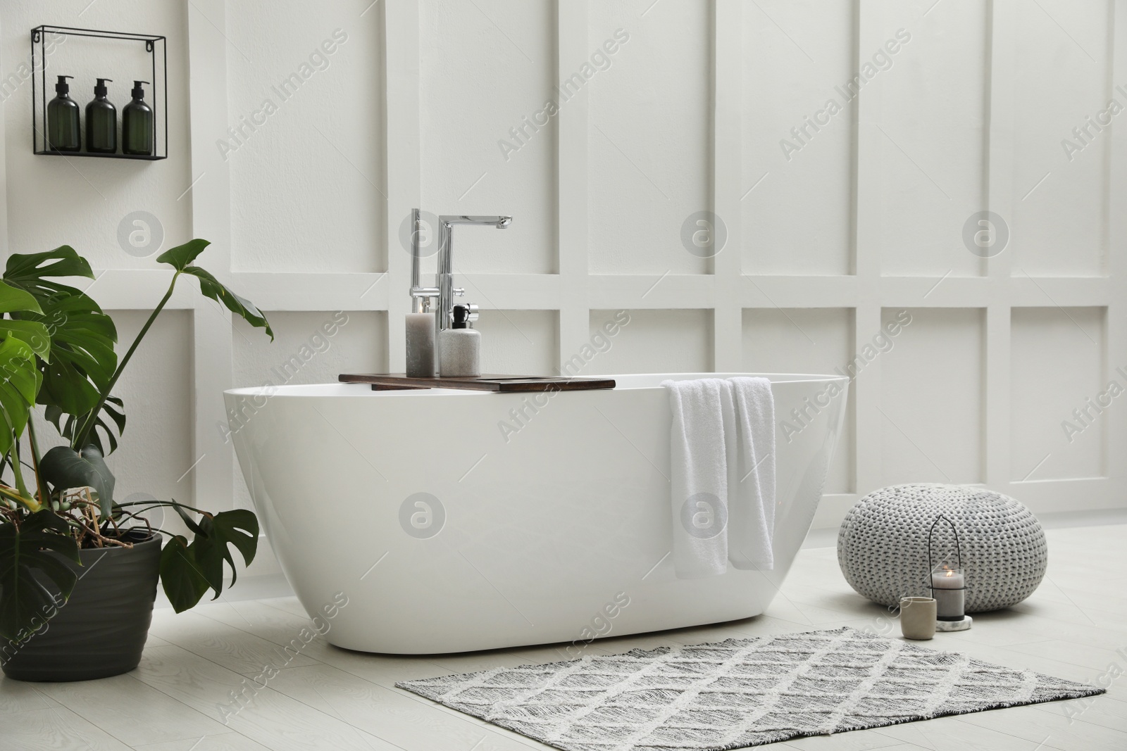 Photo of Modern ceramic bathtub and green plant near white wall indoors