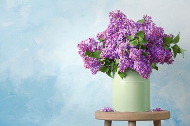 Photo of Vase with beautiful blossoming lilac on table against color background. Spring flowers