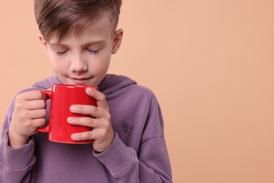 Cute boy with red ceramic mug on beige background, space for text