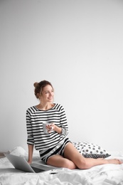 Female blogger with laptop and cup of coffee on bed