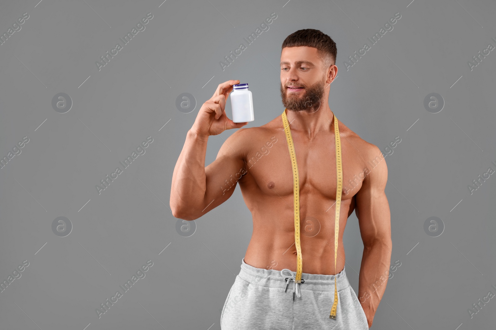 Photo of Athletic young man with measuring tape and bottle of supplements on grey background. Weight loss