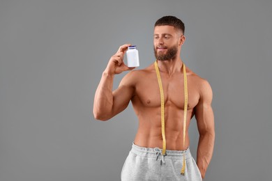 Athletic young man with measuring tape and bottle of supplements on grey background. Weight loss