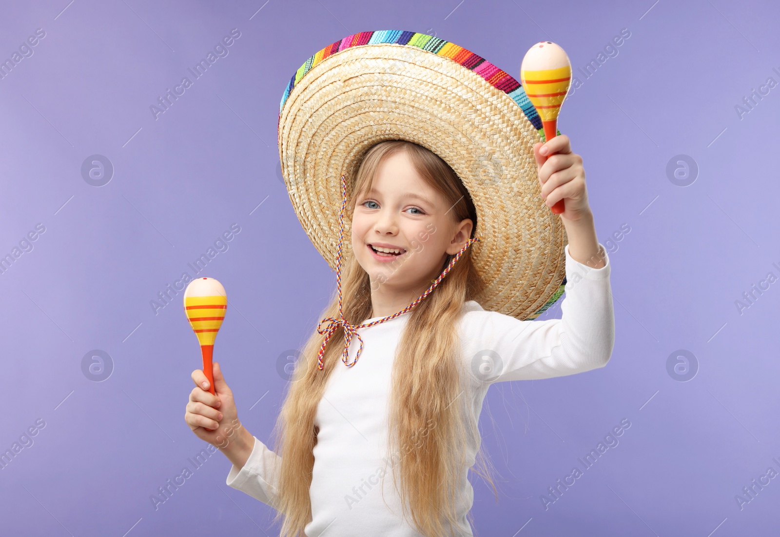 Photo of Cute girl in Mexican sombrero hat dancing with maracas on purple background