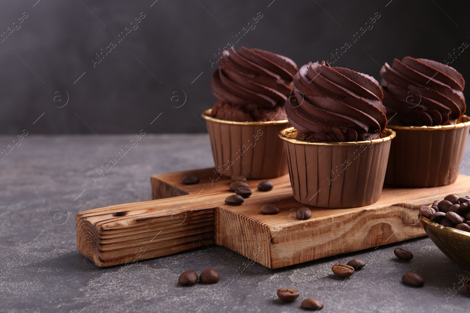 Photo of Delicious chocolate cupcakes and coffee beans on grey textured table, closeup. Space for text