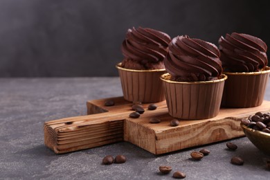 Photo of Delicious chocolate cupcakes and coffee beans on grey textured table, closeup. Space for text