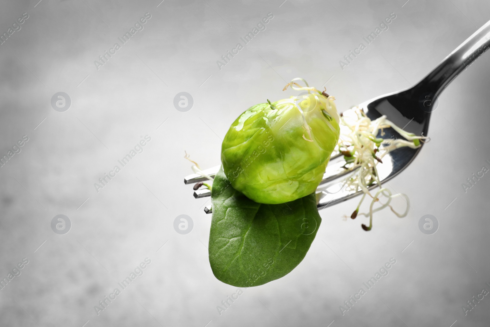 Photo of Fork with delicious Brussels sprouts salad on grey background, closeup. Space for text