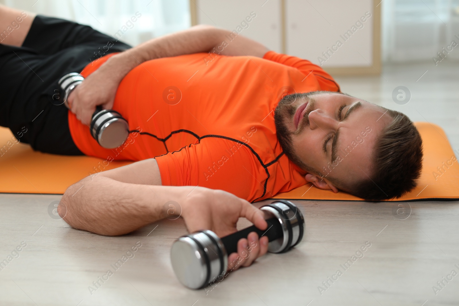 Photo of Lazy young man with sport equipment on yoga mat at home