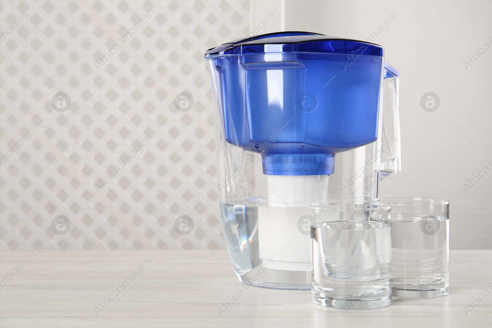 Photo of Filter jug and glasses with purified water on white table indoors. Space for text