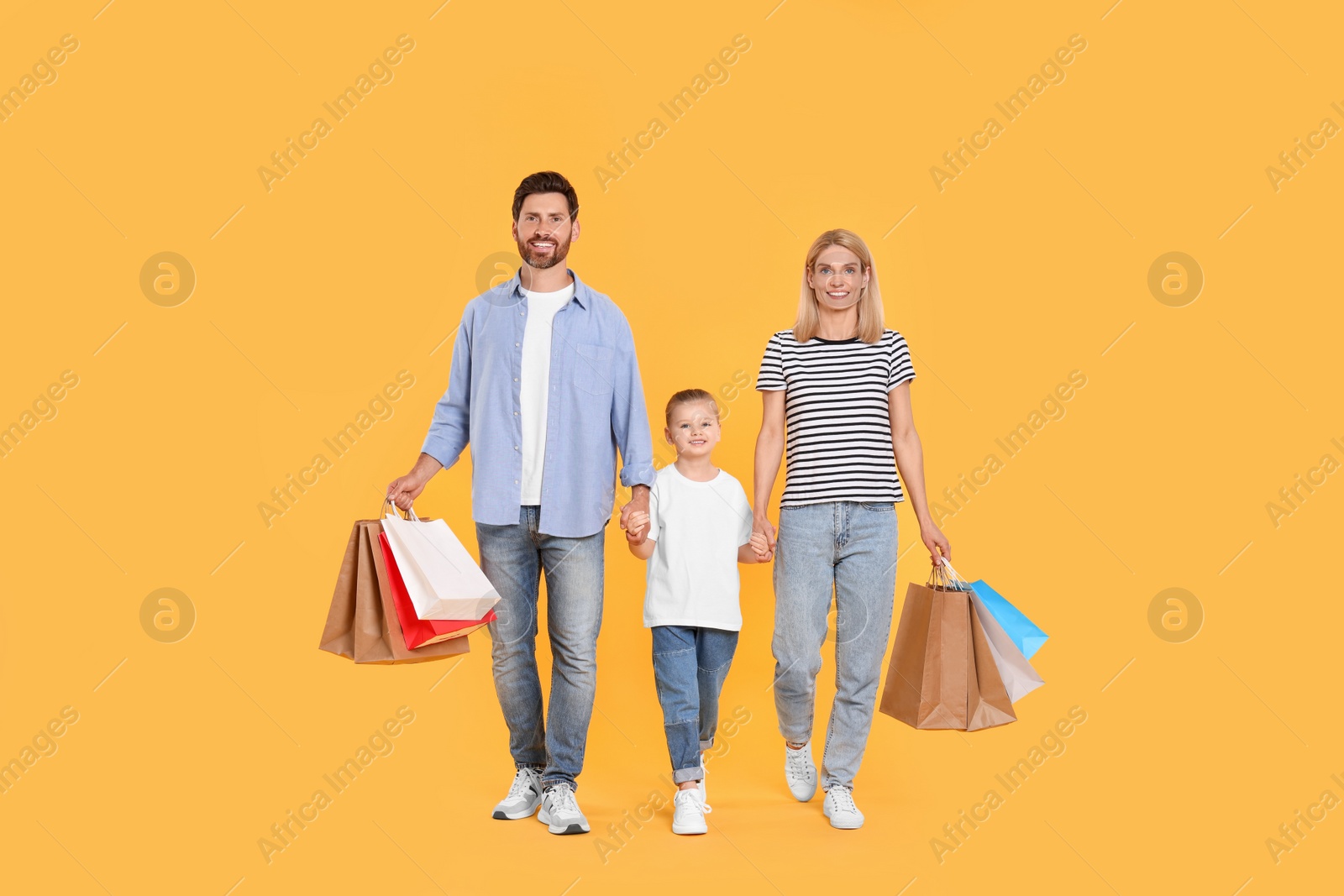 Photo of Family shopping. Happy parents and daughter with paper bags on orange background