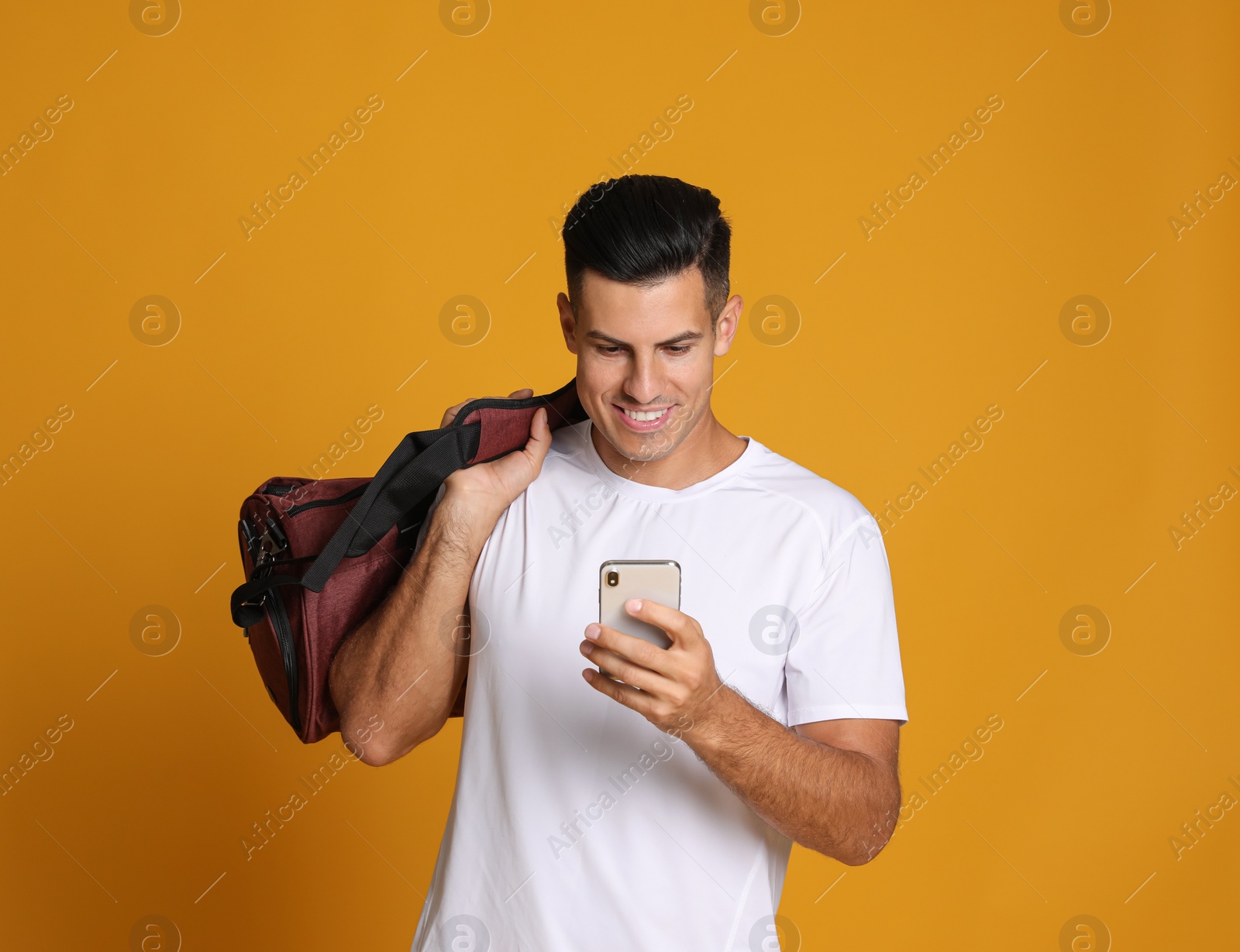 Photo of Handsome man with sports bag and smartphone on yellow background