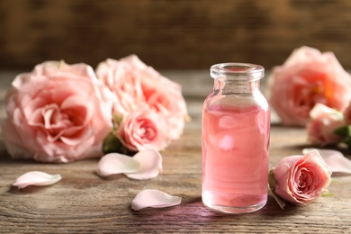 Photo of Bottle of rose essential oil and flowers on wooden table, space for text