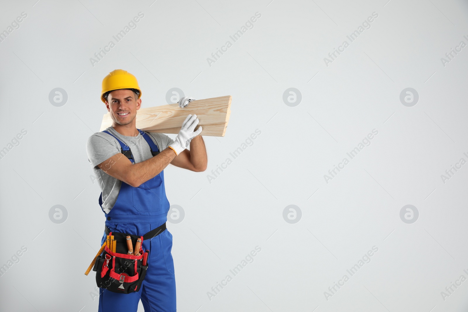 Photo of Handsome carpenter with wooden planks on light background. Space for text