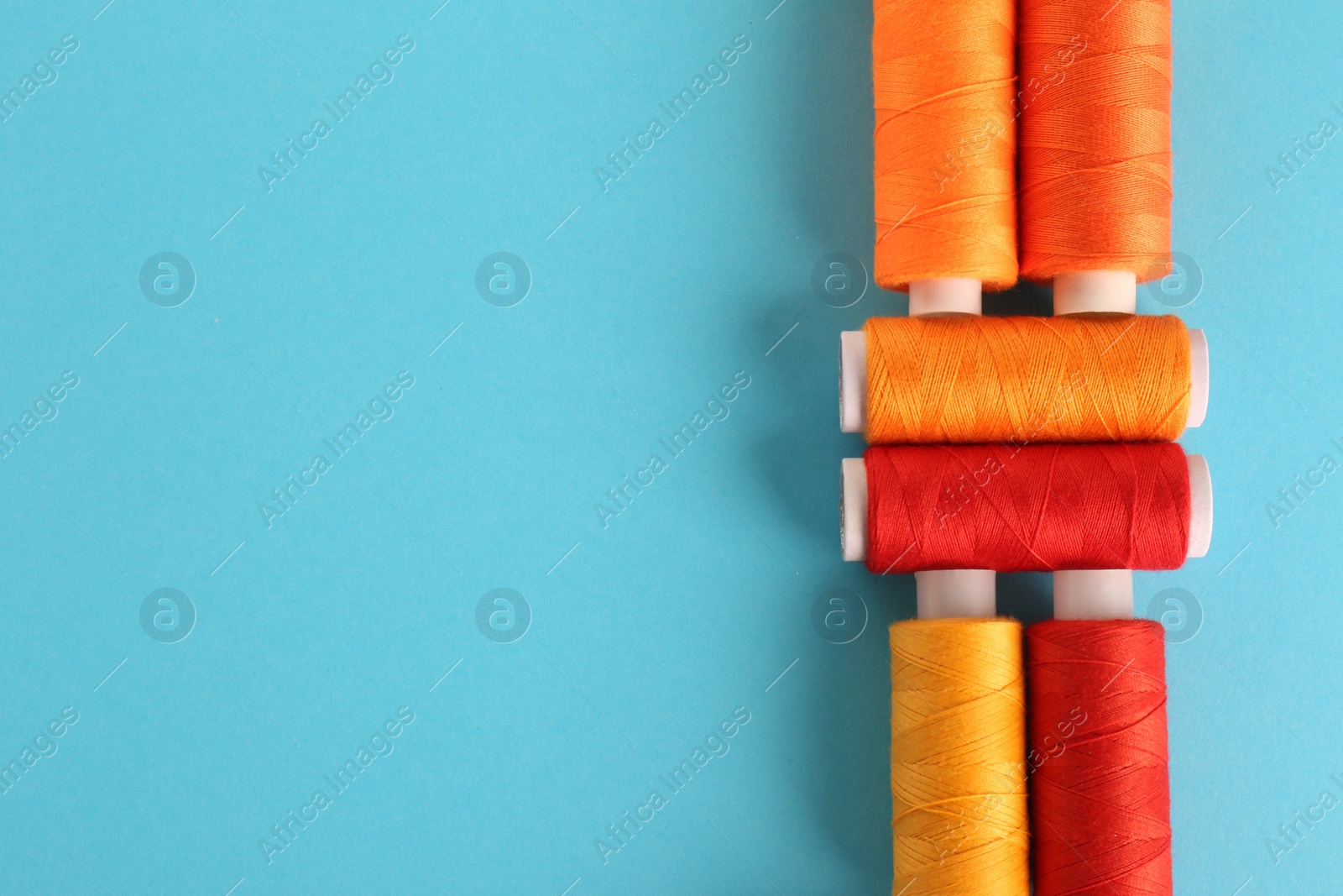 Photo of Different colorful sewing threads on light blue background, flat lay. Space for text