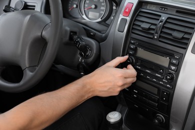 Photo of Listening to radio while driving. Man turning volume button on vehicle audio in car, closeup