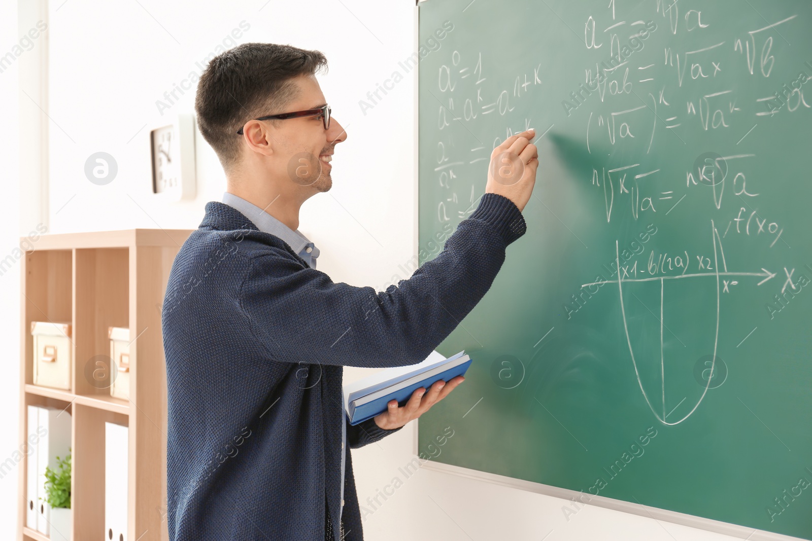 Photo of Young male teacher writing on blackboard in classroom