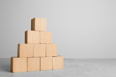 Photo of Pyramid of blank wooden cubes on grey table against light background. Space for text