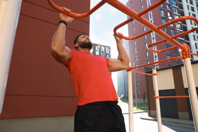 Man training on horizontal bars at outdoor gym on sunny day
