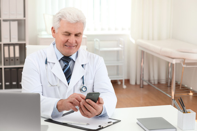 Photo of Senior doctor with smartphone at table in office
