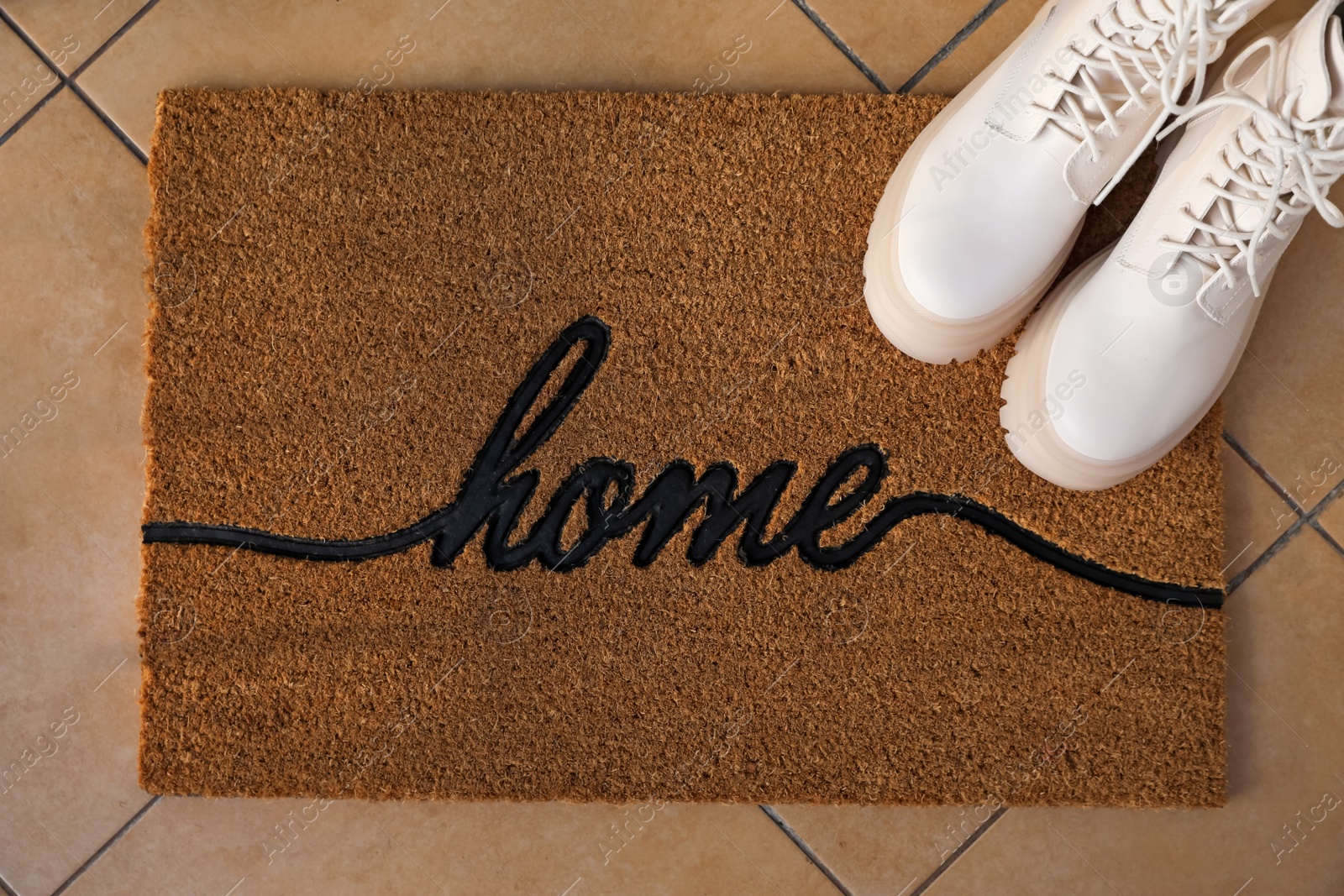 Photo of Doormat with word Home and stylish boots on tiled floor, flat lay