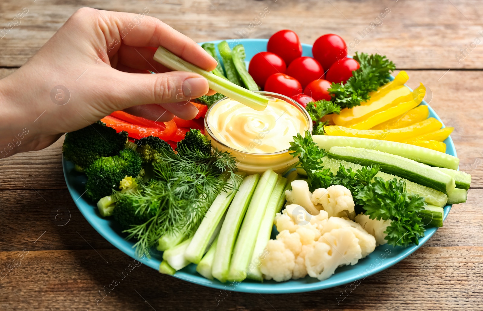 Photo of Woman dipping celery stick in sauce at wooden table, closeup