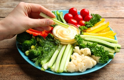 Photo of Woman dipping celery stick in sauce at wooden table, closeup