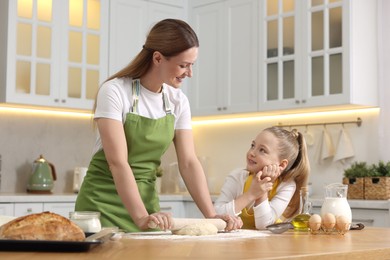 Making bread. Mother and her daughter rolling dough at wooden table in kitchen