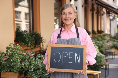 Happy business owner holding open sign near her cafe outdoors, space for text