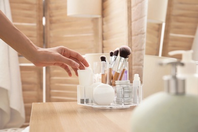 Photo of Woman taking tube with cream from organizer for cosmetic products on table