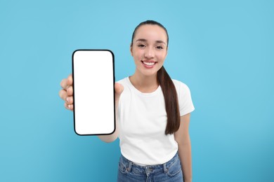 Photo of Young woman showing smartphone in hand on light blue background