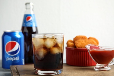 MYKOLAIV, UKRAINE - FEBRUARY 15, 2021: Glass of Pepsi and snack on wooden board, closeup