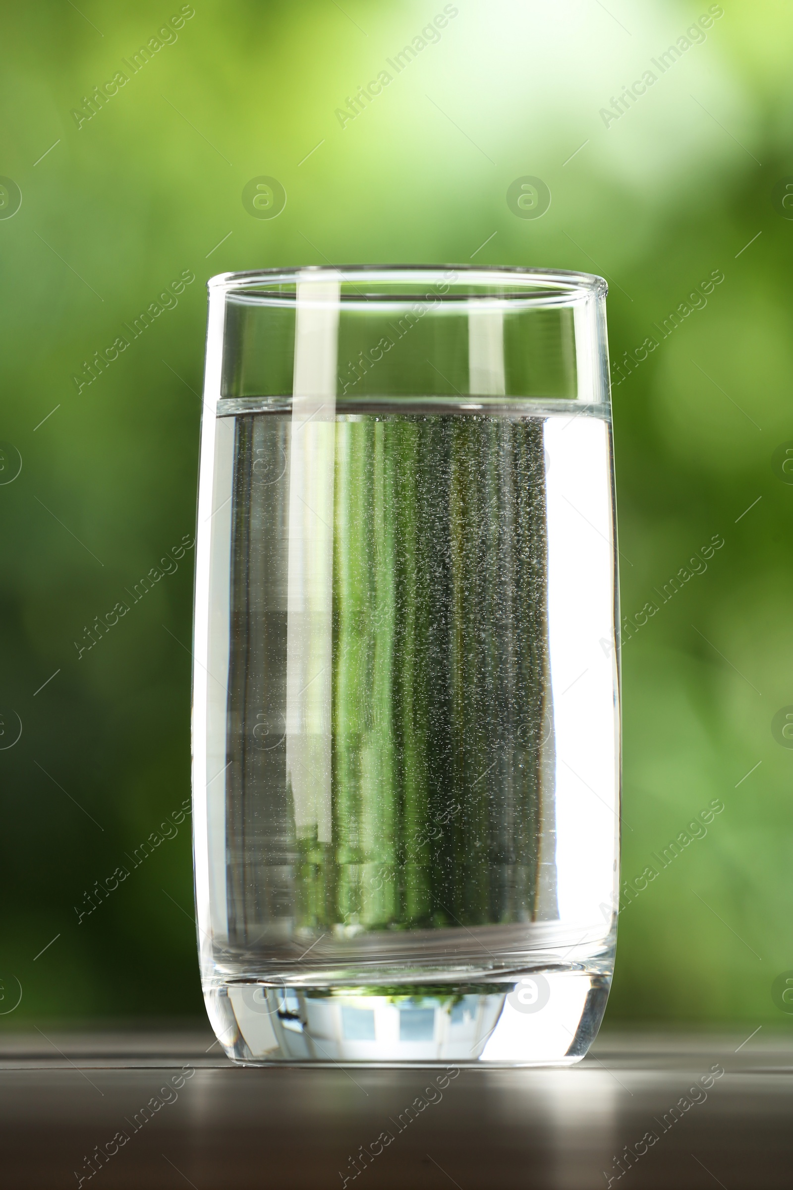 Photo of Glass of fresh water on table against blurred green background, closeup