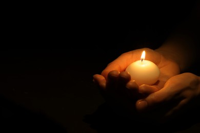 Woman holding burning candle in hands on black background, closeup. Space for text
