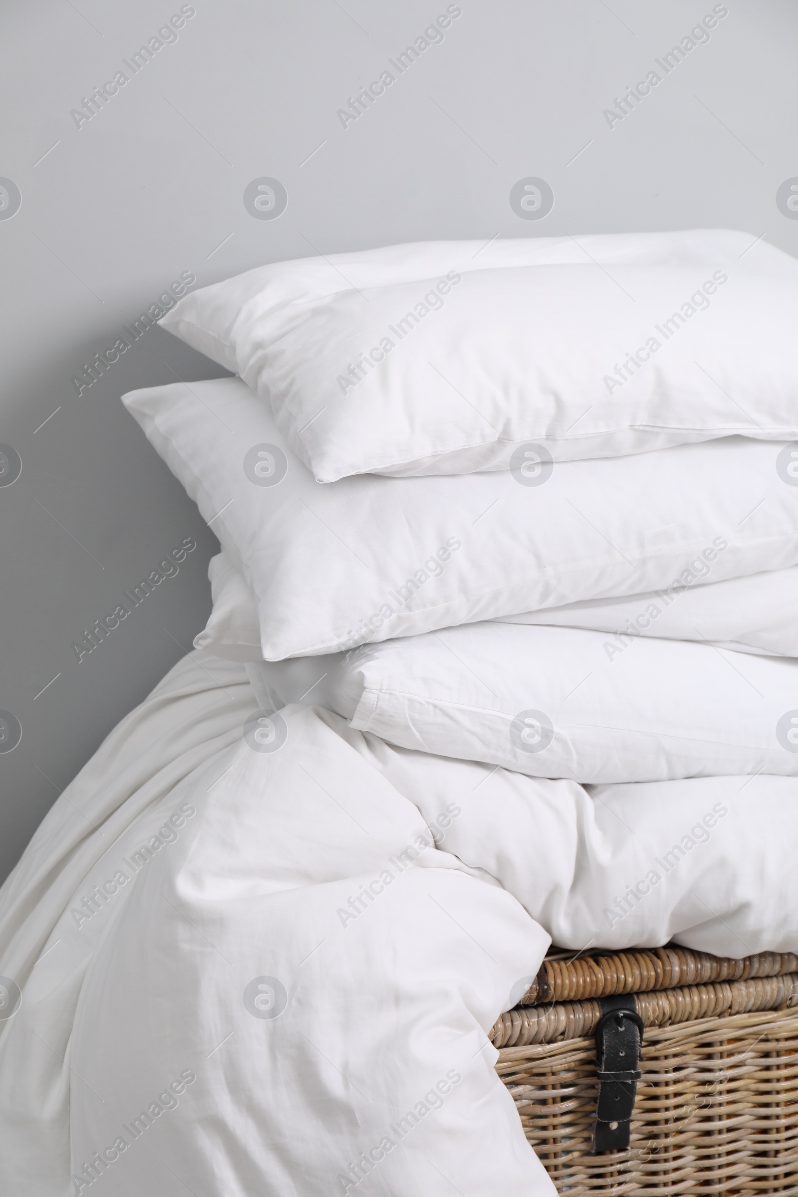 Photo of Soft pillows and duvet on wicker trunk near grey wall indoors