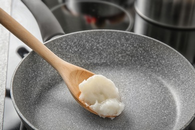 Photo of Wooden spoon with coconut oil in frying pan. Healthy cooking