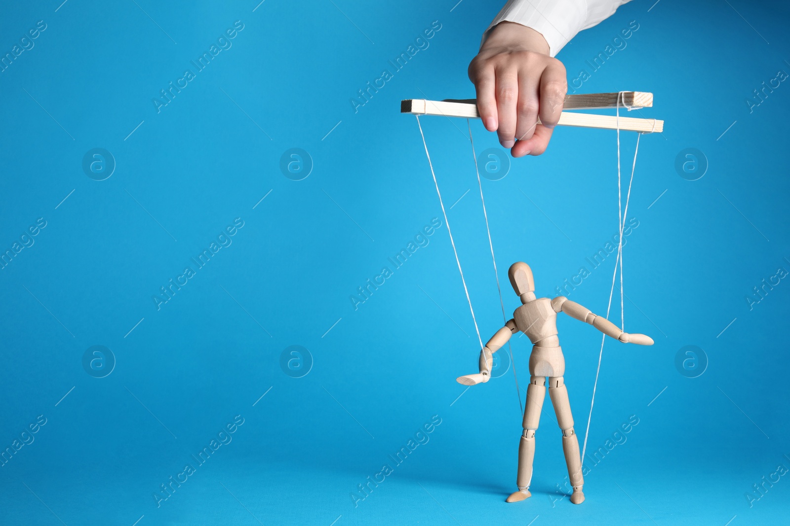 Photo of Woman pulling strings of puppet on light blue background, closeup. Space for text