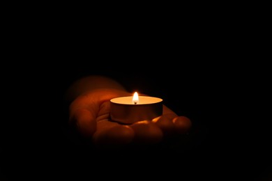 Woman holding burning candle in hand on black background, closeup