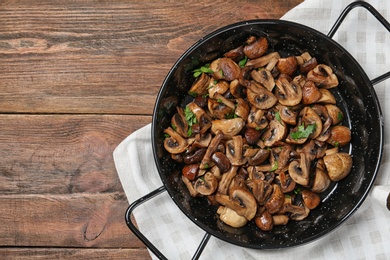 Photo of Frying pan with mushrooms on wooden background, top view. Space for text