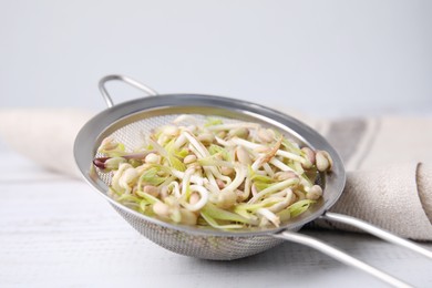 Mung bean sprouts in strainer and kitchen towel on white wooden table, closeup