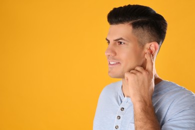 Photo of Man inserting foam ear plugs on yellow background. Space for text